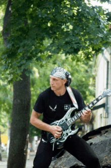 a man with a bandana on his head is playing a guitar outside