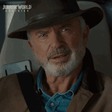 a man with a beard wearing a hat with jurassic world dominion written on it