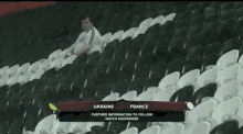 a man in a white shirt holds up his arms in the air while watching a game between ukraine and france