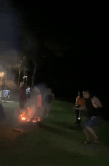 a group of people are dancing around a fire in the dark .