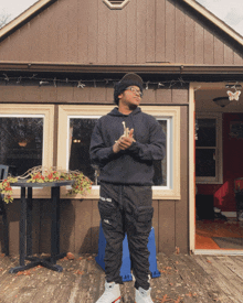 a man in a black hoodie and black pants stands in front of a brown building