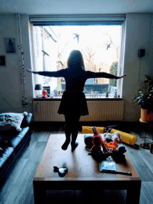 a little girl is standing on a table in front of a window with her arms outstretched