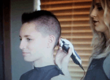 a woman is cutting a young man 's hair with a clipper