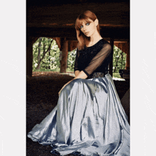 a woman wearing a black top and a silver skirt is sitting on the ground