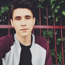 a young man is taking a selfie in front of a fence with trees in the background .