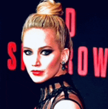 a woman with blonde hair in a bun is standing in front of a red sign that says ' show ' on it .