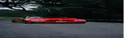 a red sports car is driving down a road with trees in the background .
