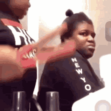 a woman is getting her hair done by a hairdresser while wearing a black shirt with the word new york on the sleeve .