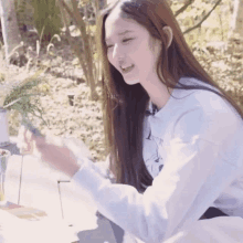 a woman with long hair is sitting at a table in the woods smiling .