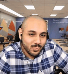 a bald man with a beard is wearing headphones and a plaid shirt while sitting in a chair .