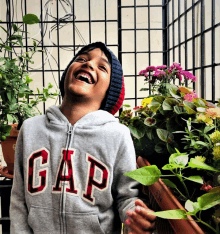 a boy wearing a gap sweatshirt is laughing in front of flowers