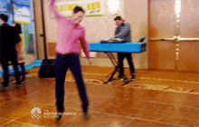 a man in a pink shirt is dancing on a dance floor with the winter olympics logo in the background