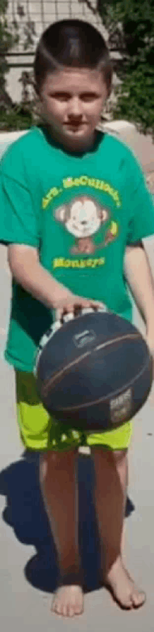 a young boy in a green shirt with a monkey on it holds a basketball