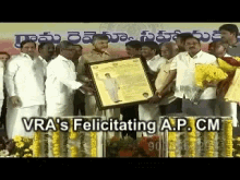 a group of men holding a framed picture with the words vra 's felicitating a.p. cm on the bottom right