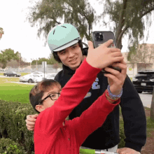 a man wearing a helmet takes a selfie with a boy wearing a red shirt with the letter c on it