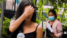 a woman in a black tank top is covering her face with her hand while holding a cup of coffee .