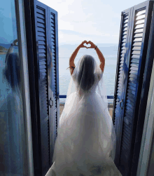 a woman in a wedding dress is making a heart with her hands