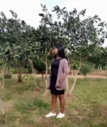 a woman in a black dress is standing in front of a tree in a field