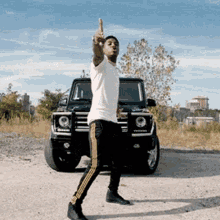 a man in a white shirt and black pants is standing in front of a jeep and giving the middle finger