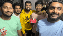 a group of young men are posing for a picture and one of them is holding a birthday cake