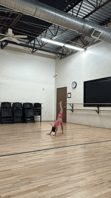 a girl in a pink top is doing a handstand on a wooden floor