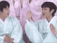 two young men in white kimonos are sitting next to each other and clapping .