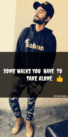 a man wearing a hoodie that says soban stands in front of a sign that says some walks you have to take alone