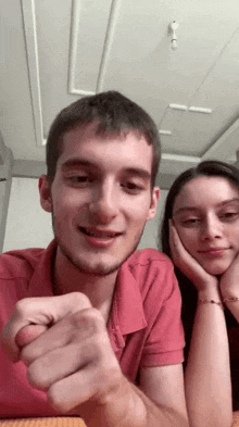 a man and woman are sitting at a table with their hands on their faces . the man is wearing a red shirt .