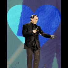 a man in a black suit is pointing at a blue heart