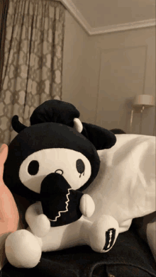 a person is holding a black and white stuffed animal that looks like a demon