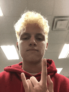 a young man with blonde hair and a red hoodie giving the middle finger