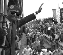 a man wearing sunglasses and a military hat waves to a crowd