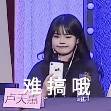 a young woman is sitting at a table holding a cell phone .