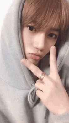 a young man wearing a hoodie and a ring on his finger is making a peace sign