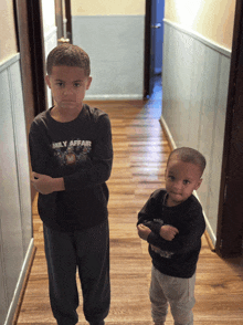 a boy wearing a daily affair shirt stands next to another boy in a hallway