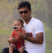 a man is holding a baby wearing sunglasses and a shirt that says ' ayo ' on it