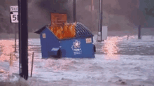 a dumpster is floating in a flooded area near a highway sign