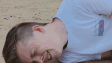 a young man laying on the ground with his eyes closed and a white shirt with a purple and blue graphic on it