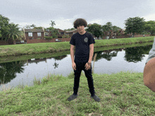 a man wearing a black shirt that says anti social social club stands in front of a body of water