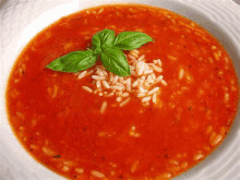 a bowl of tomato soup with rice and basil on top of it .