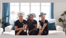 three women sitting on a white couch wearing cat shirts and hats