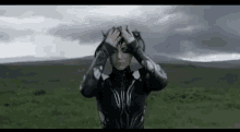 a woman in a superhero costume is standing in a field holding her head .