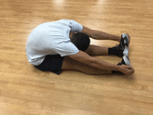 a man in a white shirt is stretching his legs on a wooden floor