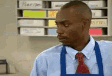 a man wearing a blue apron and a red tie stands in front of a shelf with sticky notes on it