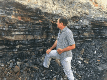 a man in a striped shirt is standing in front of a large pile of rocks