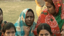 a group of women are standing in a field and one of them is wearing a blue and white checkered scarf