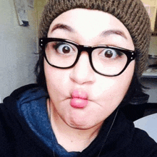 a woman wearing glasses and a beanie is making a face