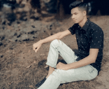 a young man in a black shirt sits on the grass