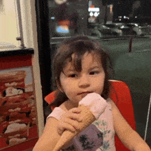 a little girl is eating an ice cream cone in front of a container that says thrilly