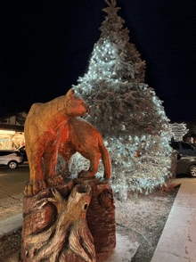 a statue of a bear on a tree stump in front of a christmas tree